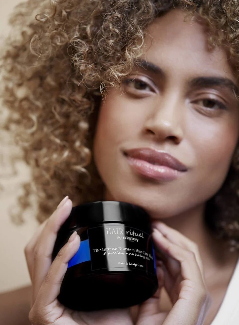 Intense Nourishment Hair Care Mask jar held by coily-haired model