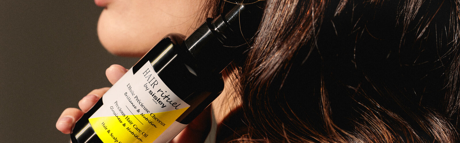 Female model holding an open bottle of Precious Hair Care Oil in her hand